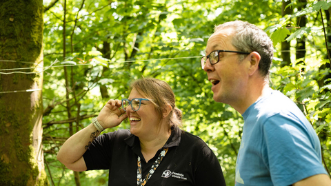 A member of Cumbria Wildlife Trust staff and a member of the public laughing together in a woodland