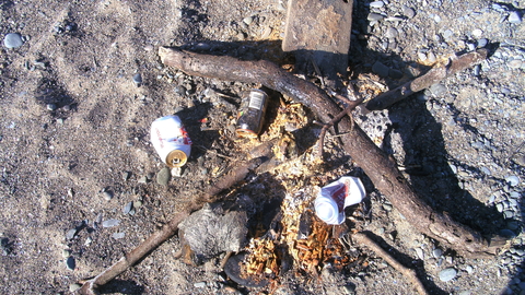 Remnants of a campfire on the beach, including cans & bottles