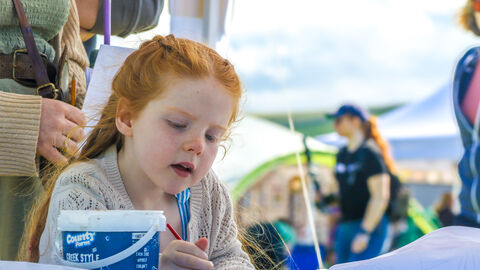 A child taking part in a crafting activity at an event, with stalls in the background