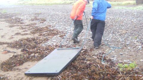 Large slab of solid plastic being towed from the beach by volunteers