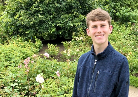 A young man in a fleece standing in front of garden greenery