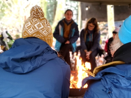 camp fire with people wearing bobble hats