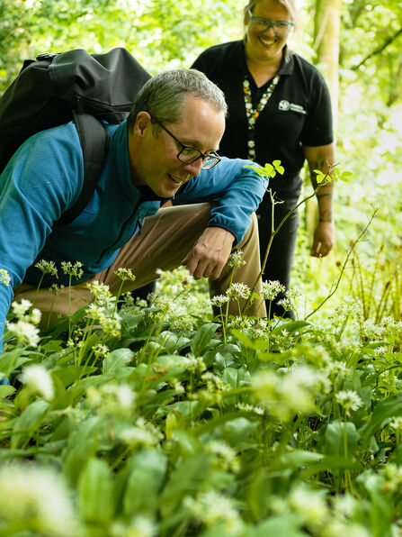 A visitor and group leader looking at greenery of the woodland floor 