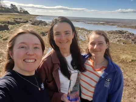 Image of three marine conservationists on beach with award