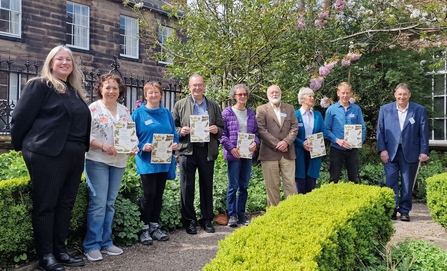 Group of volunteers holding certificates for Badger's Paw Award in garden of Tullie