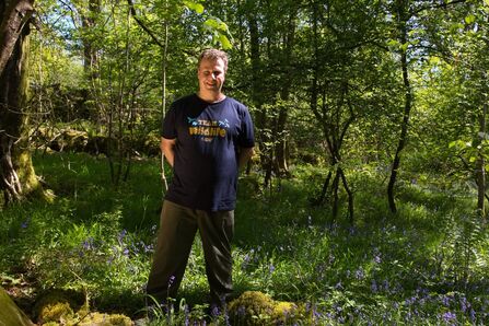 Jamie Normington standing in wood surrounded by bluebells