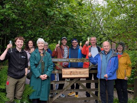Group of people surround wooden sign for new Victoria Wood Nursery, Plumgarths