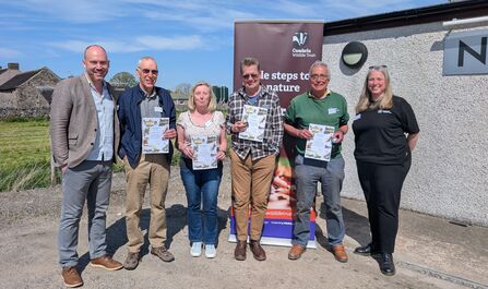Group of men and women hold up Badger's Paw award certificates in front of Cumbria Wildlife Trust banner