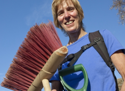 Image of Woman volunteer holding conservation tools and broom