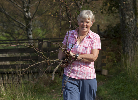 Image of a woman volunteer smiling and holding sticks outdoors