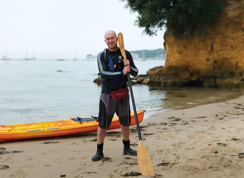 Dan stands on a beach with his kayak