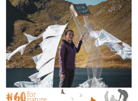 A girls standing near a lake in the mountains with a sculpture made from wire and fabric.