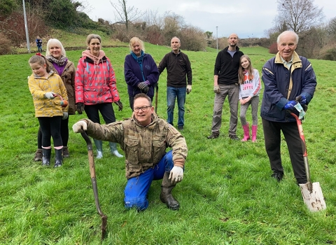 A group of people of various ages standing in a field, holding gardening tools