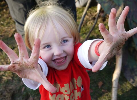 child with muddy hands wearing a Wildlife Trust Wildife Watch tee shirt