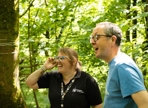 A member of Cumbria Wildlife Trust staff and a member of the public laughing together in a woodland