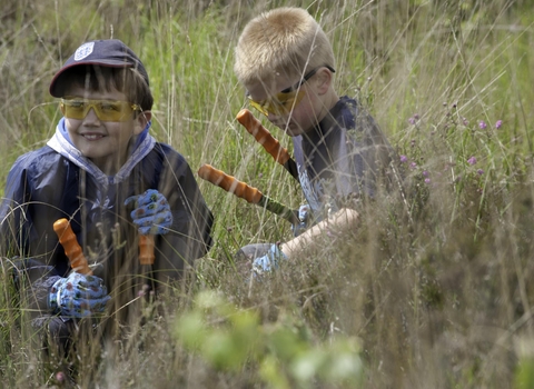 two chidren outdoors wearing protective goggles and gloves and holding gardneing sheers