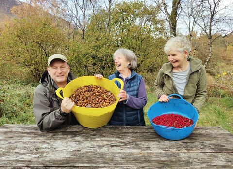Three people showing two buckets full of tree seeds collected in Borrowdale
